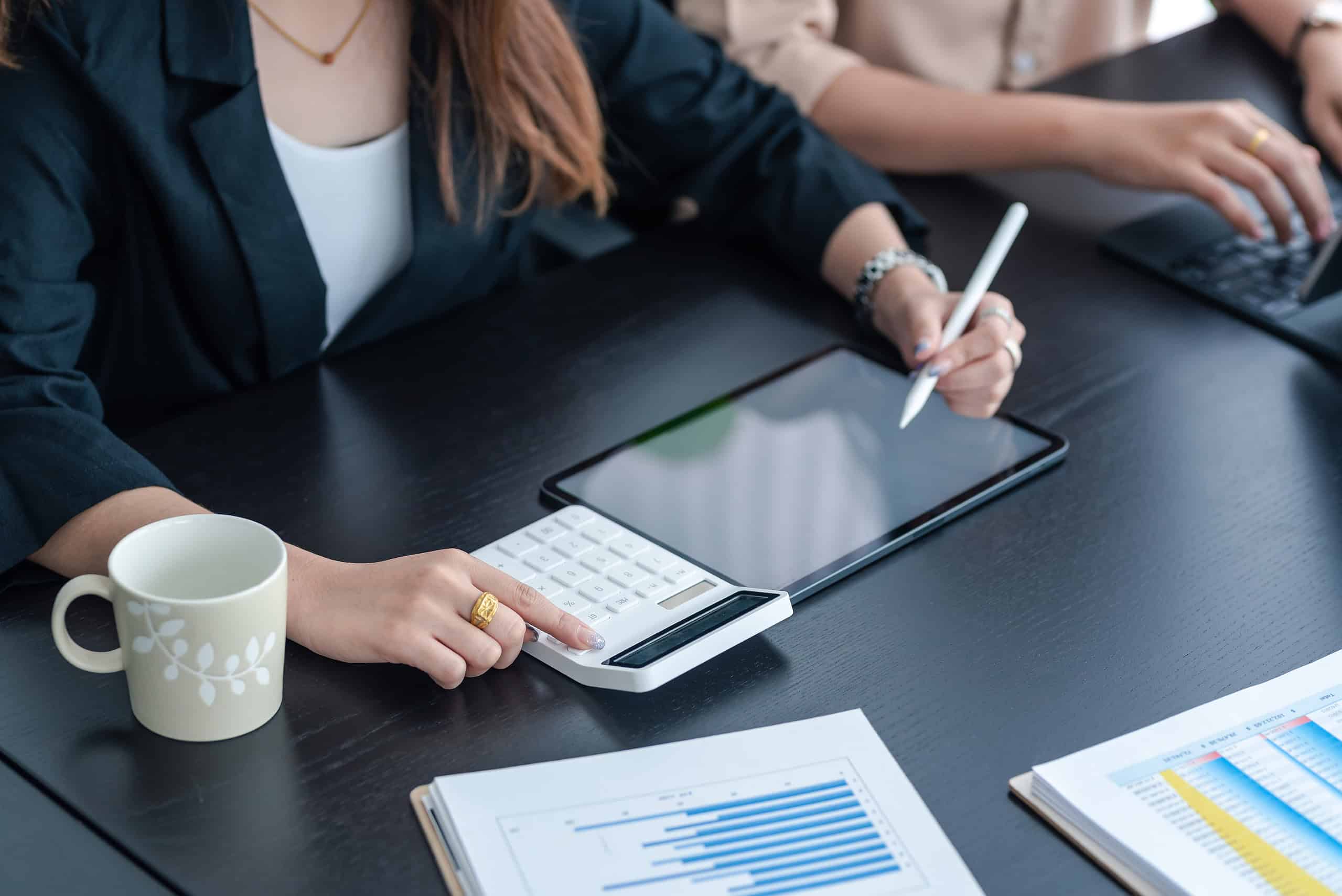 Close up of woman working at the office using a tablet and calculator and graph.